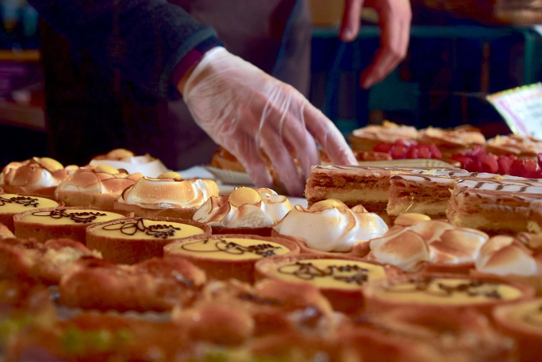 Étal de pâtissier garni de tartes au citron meringuées et de mille-feuilles, une main gantée prenant une part